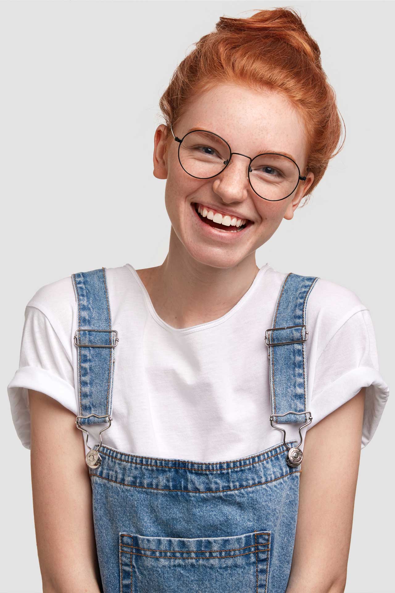 Woman with red hair and glasses wearing overalls smiling for the camera