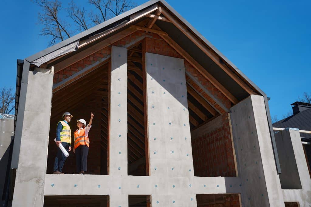 A female and male construction worker standing on the wall of a construction wall discussing the plans