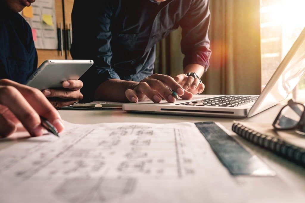 two men working on blueprints with a laptop and tablet