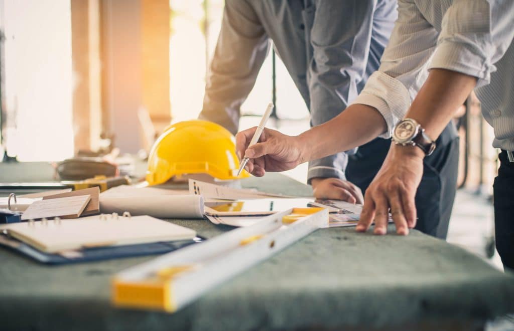 businessmen with hard hats and levelers looking at blueprints